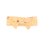 Yellow headband with a bow and pink heart designs on a white background
