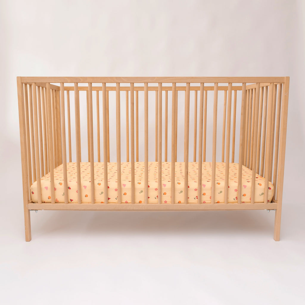 Wooden crib with a yellow patterned mattress on a white background