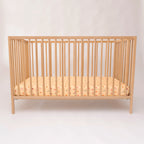 Wooden crib with a yellow patterned mattress on a white background