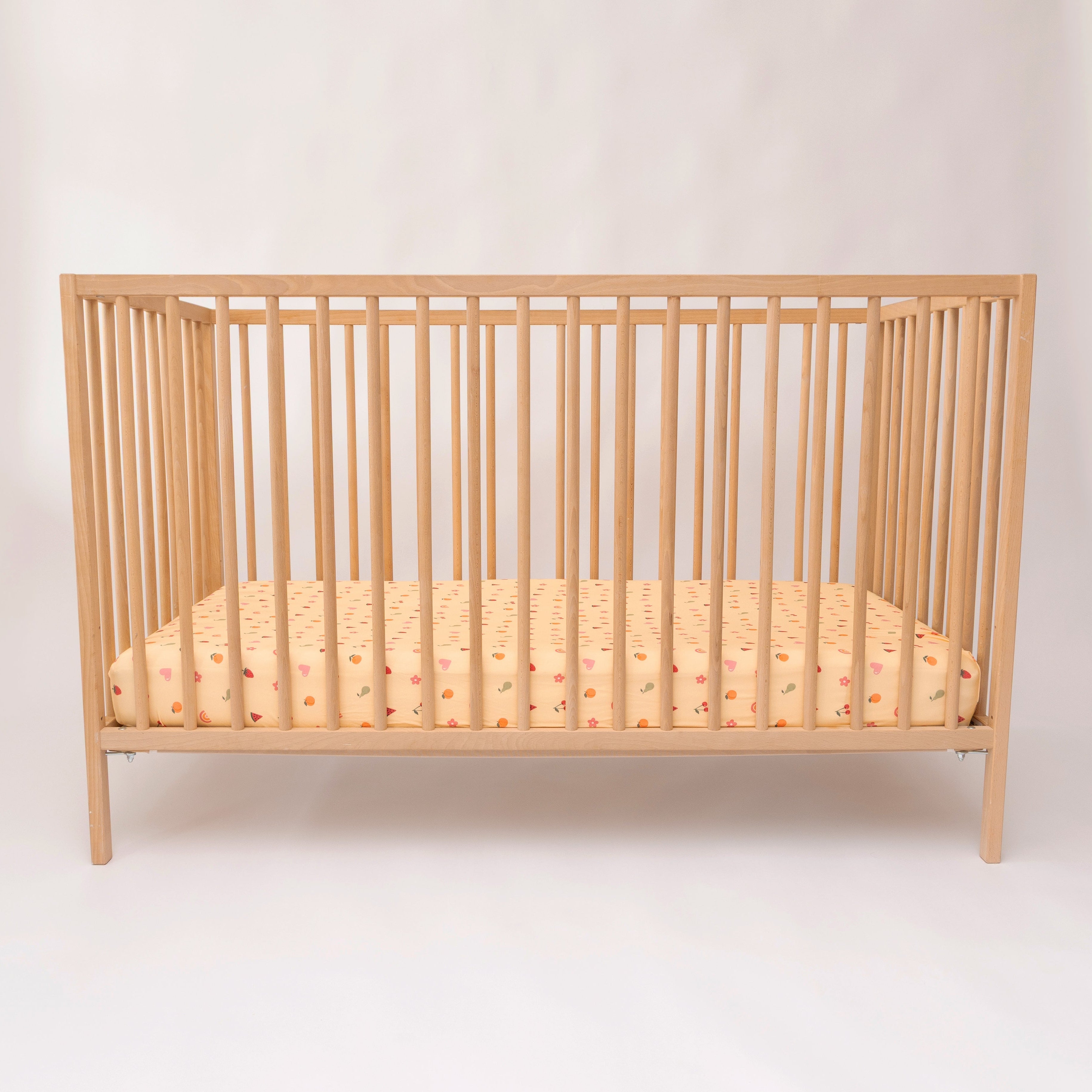 Wooden crib with a yellow patterned mattress on a white background