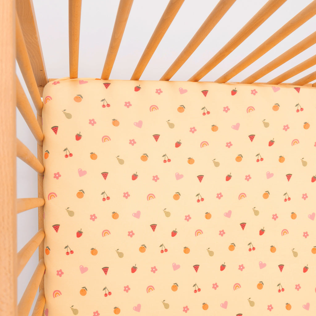 Yellow fitted sheet with colorful patterns on a wooden crib