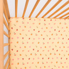 Yellow fitted sheet with colorful patterns on a wooden crib
