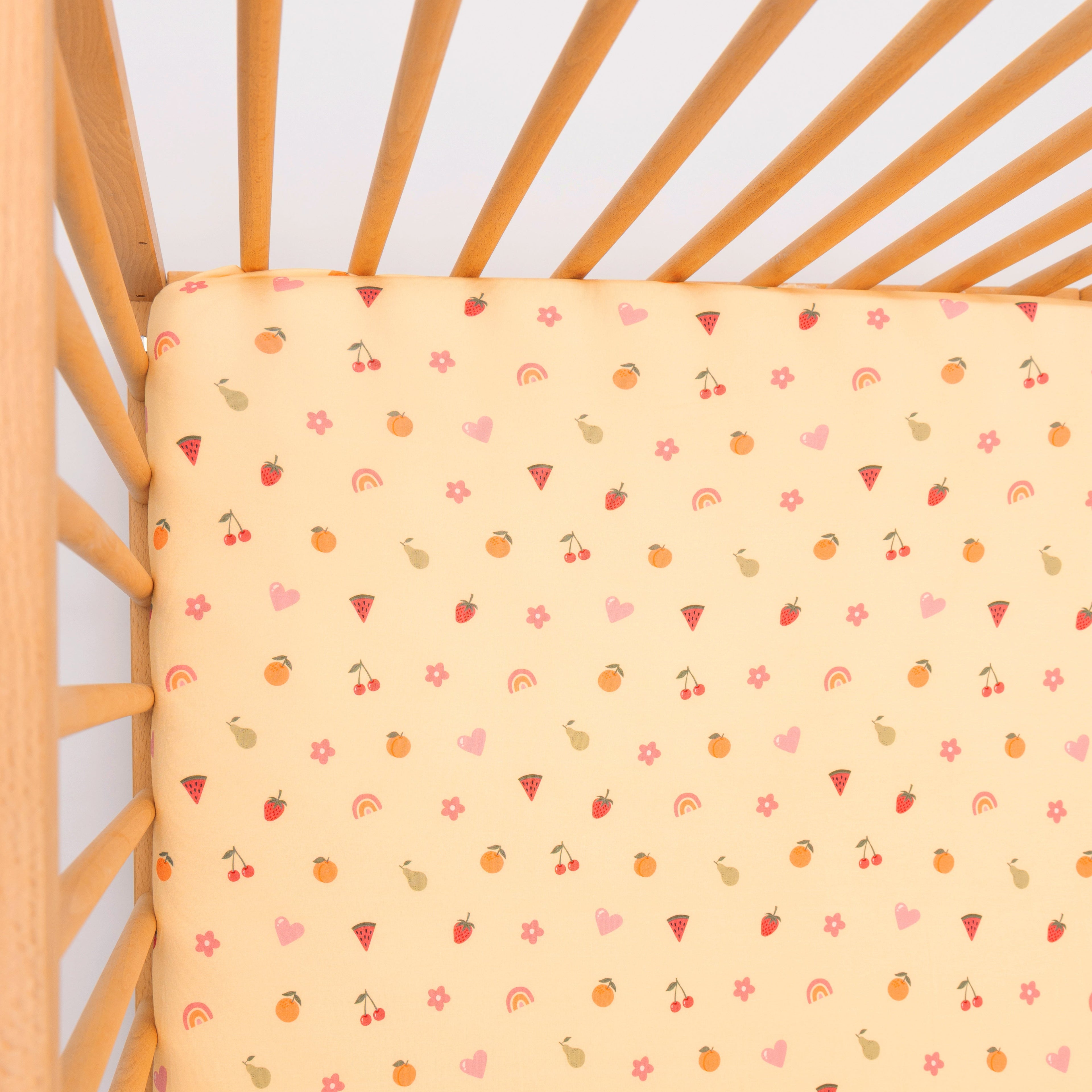 Yellow fitted sheet with colorful patterns on a wooden crib