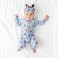 Baby wearing a blue checkered onesie with red cherries on a white textured background