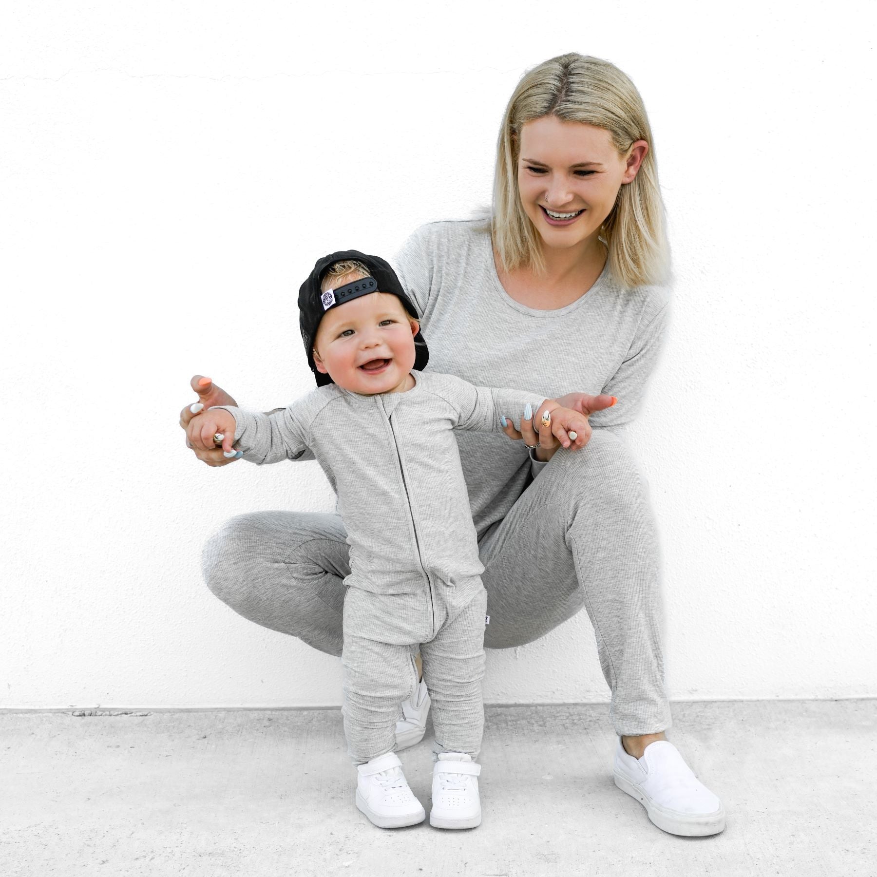 Woman and baby wearing matching gray pajama sets on a white background