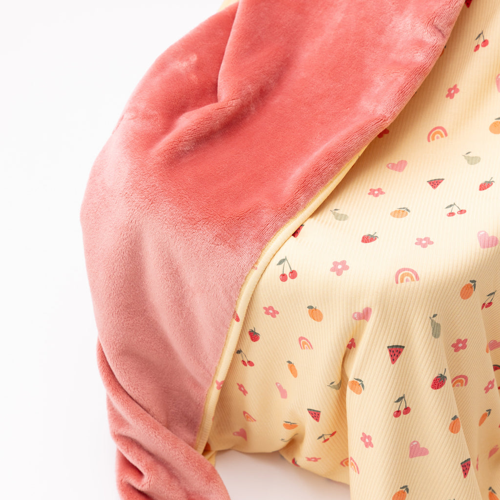 Close up of a baby blanket with colorful fruit pattern on one side and solid color on the other draped over a chair