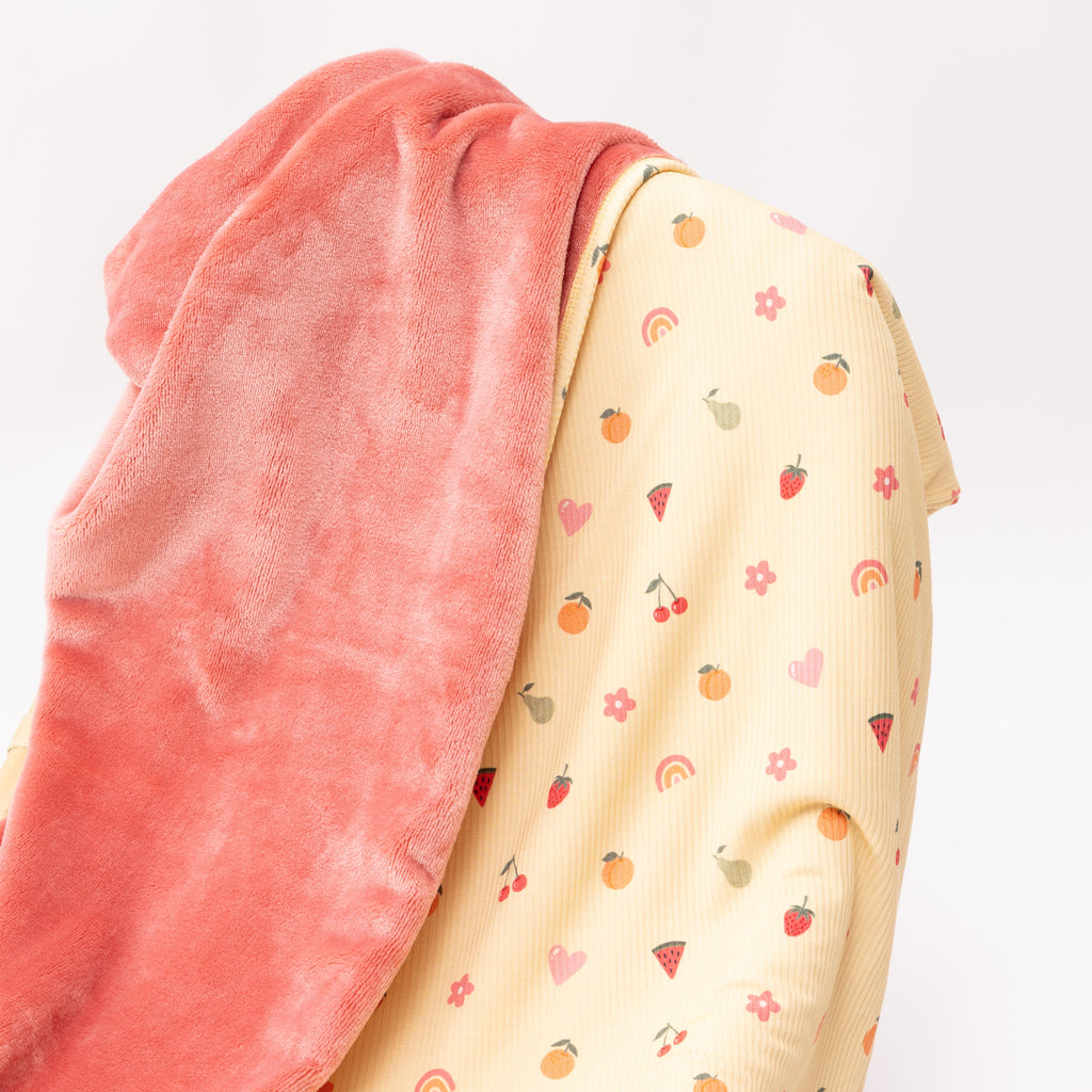 Close up of a baby blanket with colorful fruit pattern on one side and solid color on the other draped over a chair