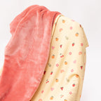 Close up of a baby blanket with colorful fruit pattern on one side and solid color on the other draped over a chair
