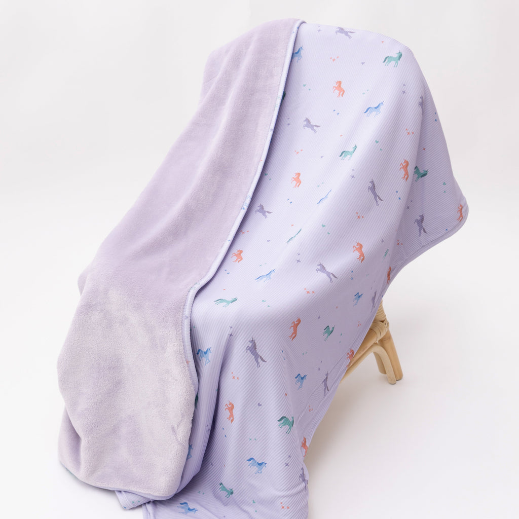 Light purple baby blanket with colorful unicorn patterns on a white background