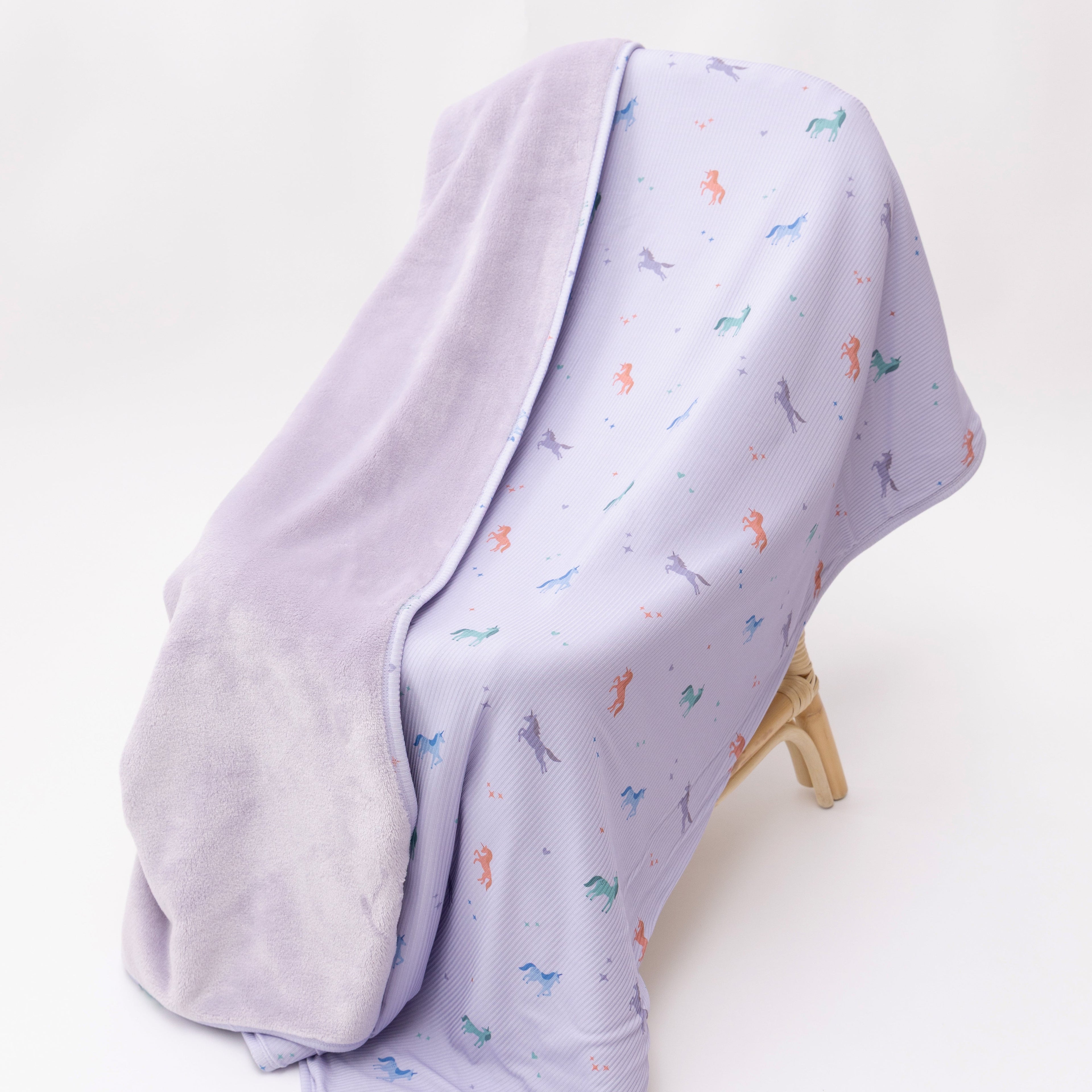 Light purple baby blanket with colorful unicorn patterns on a white background