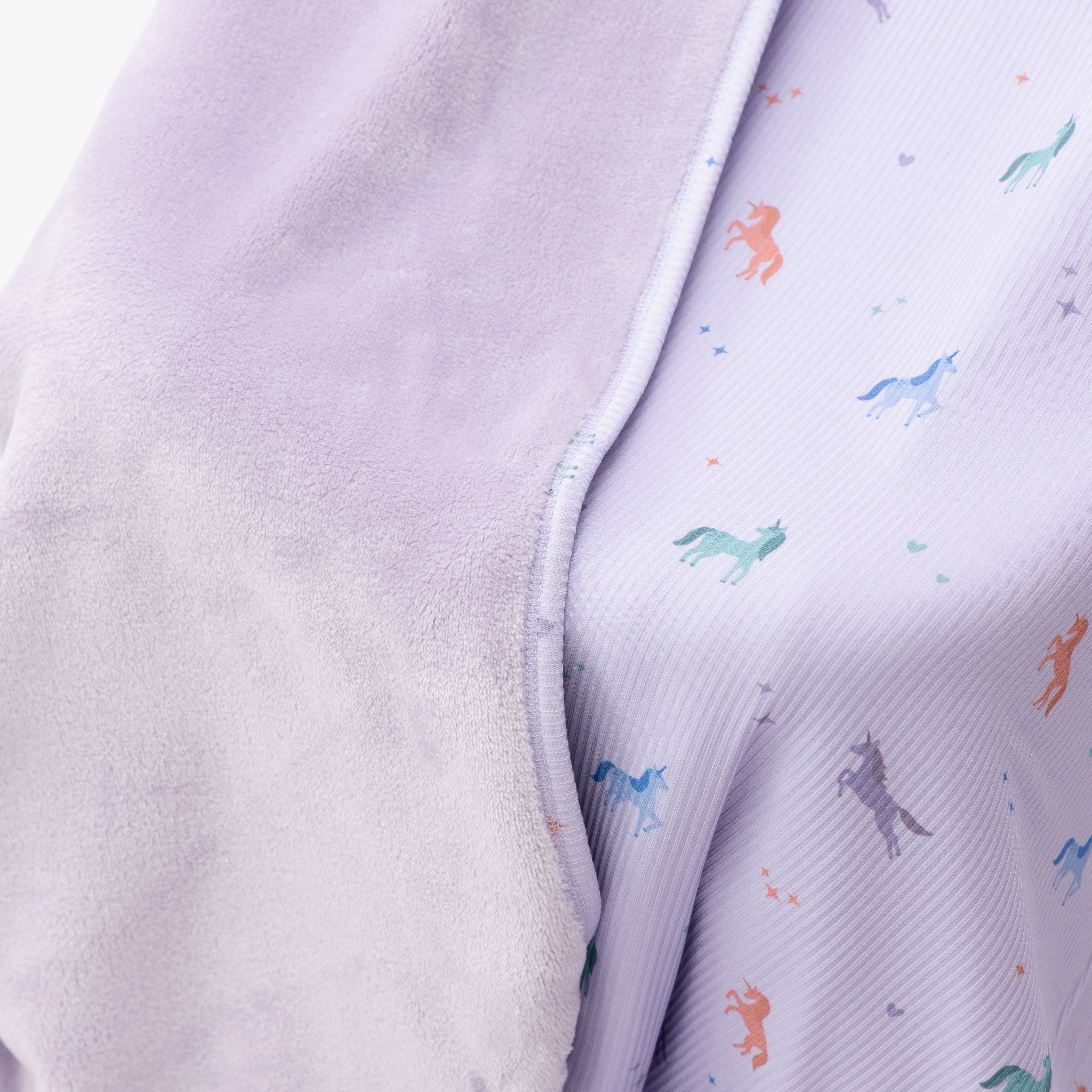 Close up shot of a light purple baby blanket with colorful unicorn patterns on a white background
