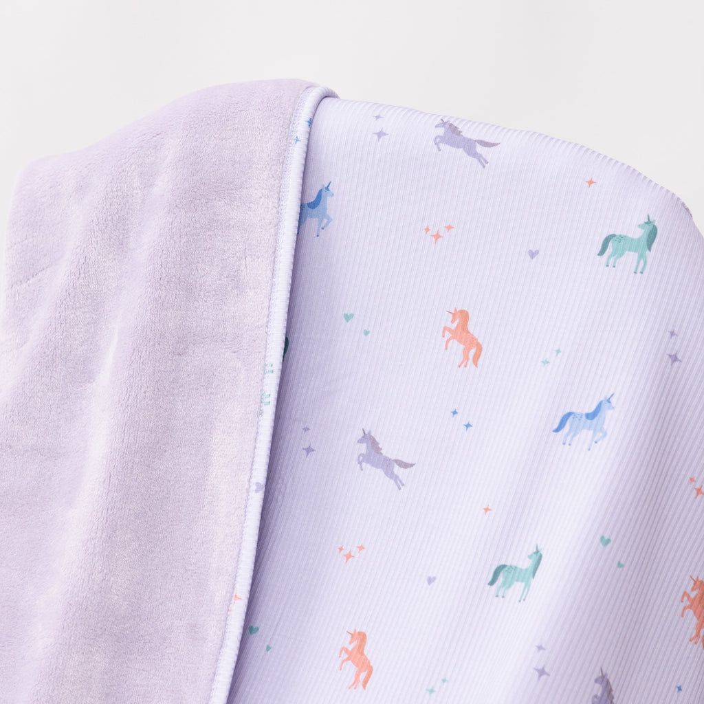 Close up shot of a light purple baby blanket with colorful unicorn patterns on a white background