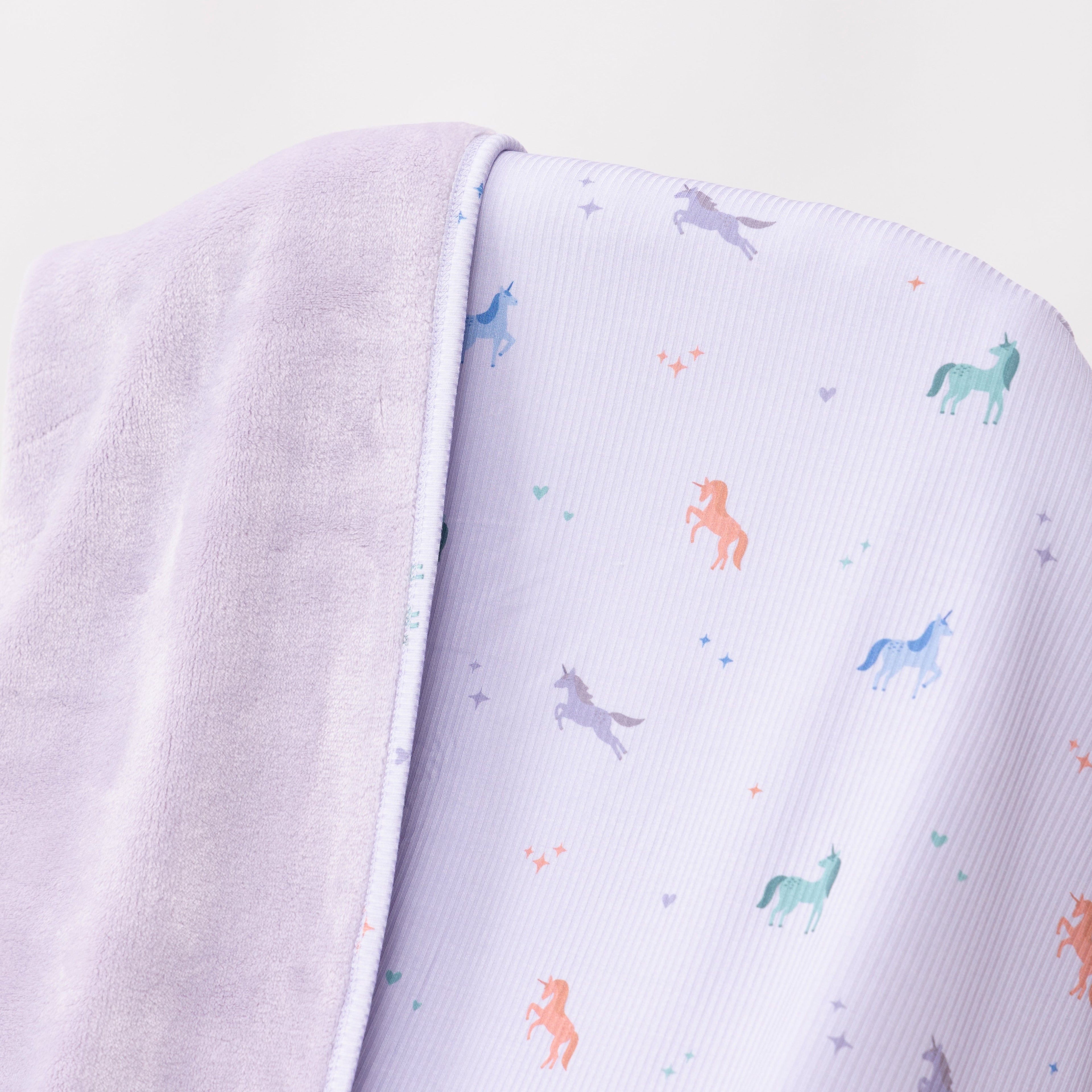 Close up shot of a light purple baby blanket with colorful unicorn patterns on a white background