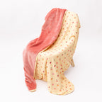 Baby blanket with colorful fruit pattern on one side and solid color on the other draped over a chair