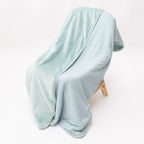 Light blue striped blanket draped over a wooden chair on a white background