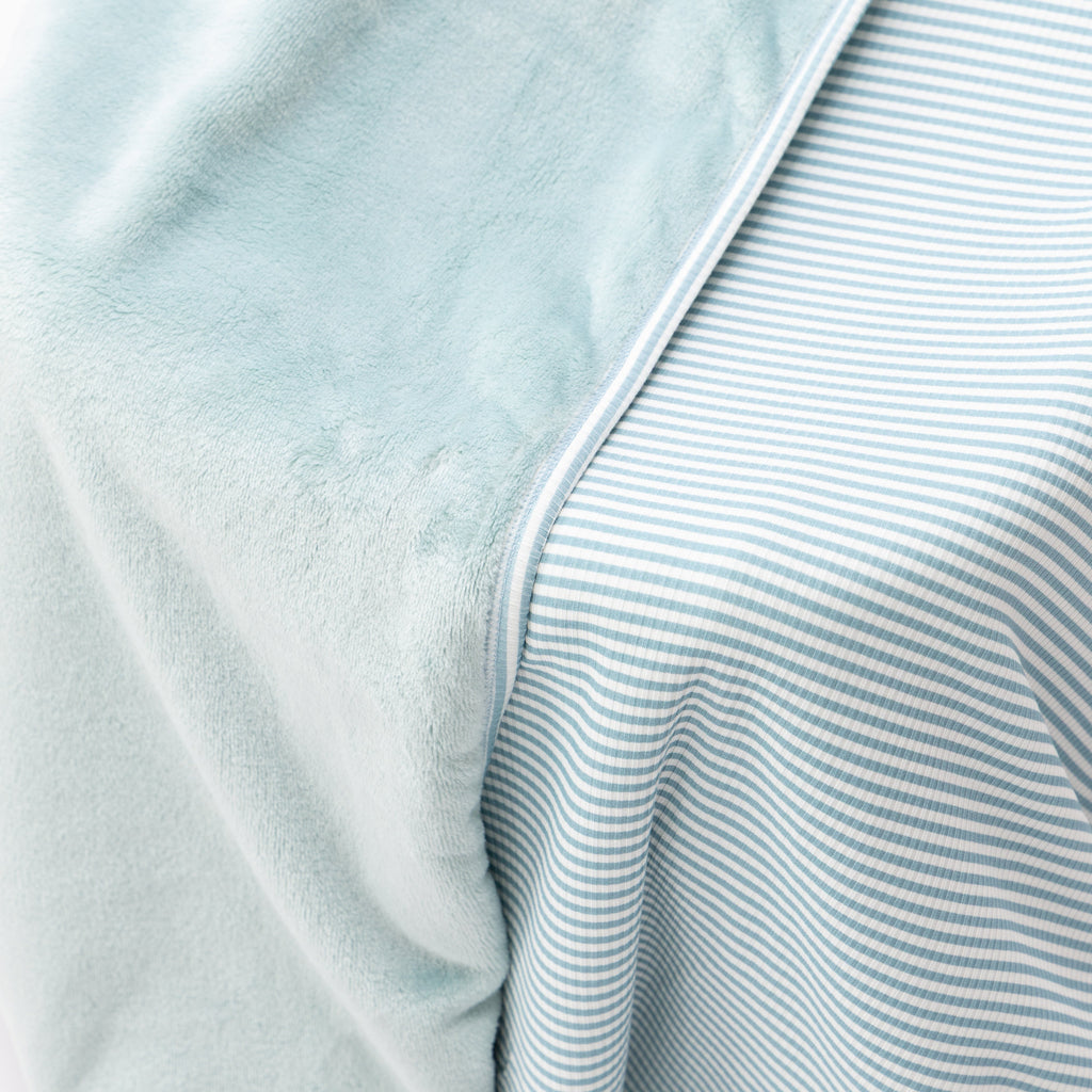 Close up of a light blue striped blanket draped over a wooden chair on a white background