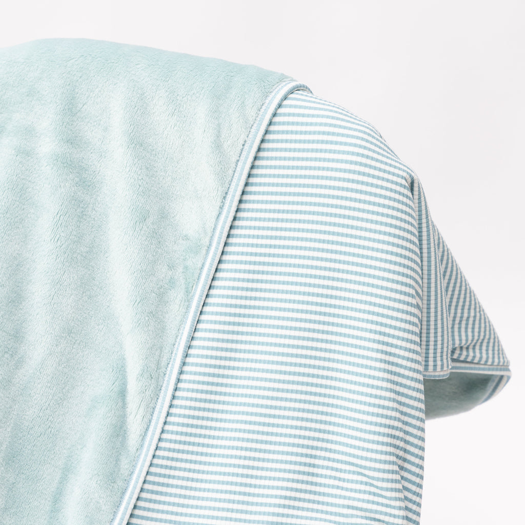 Close up of a light blue striped blanket draped over a wooden chair on a white background