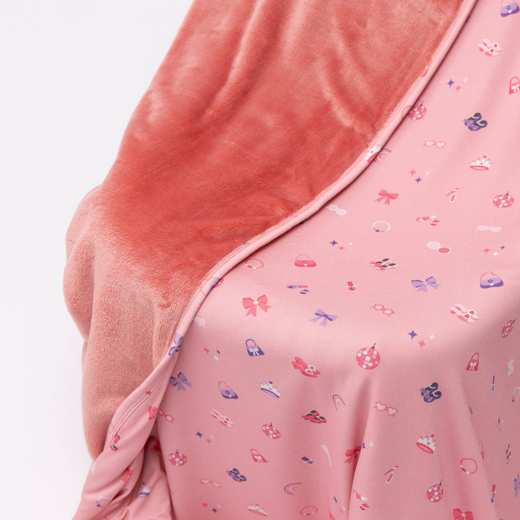 Close up of a pink blanket with small girly patterns draped over a chair on a white background