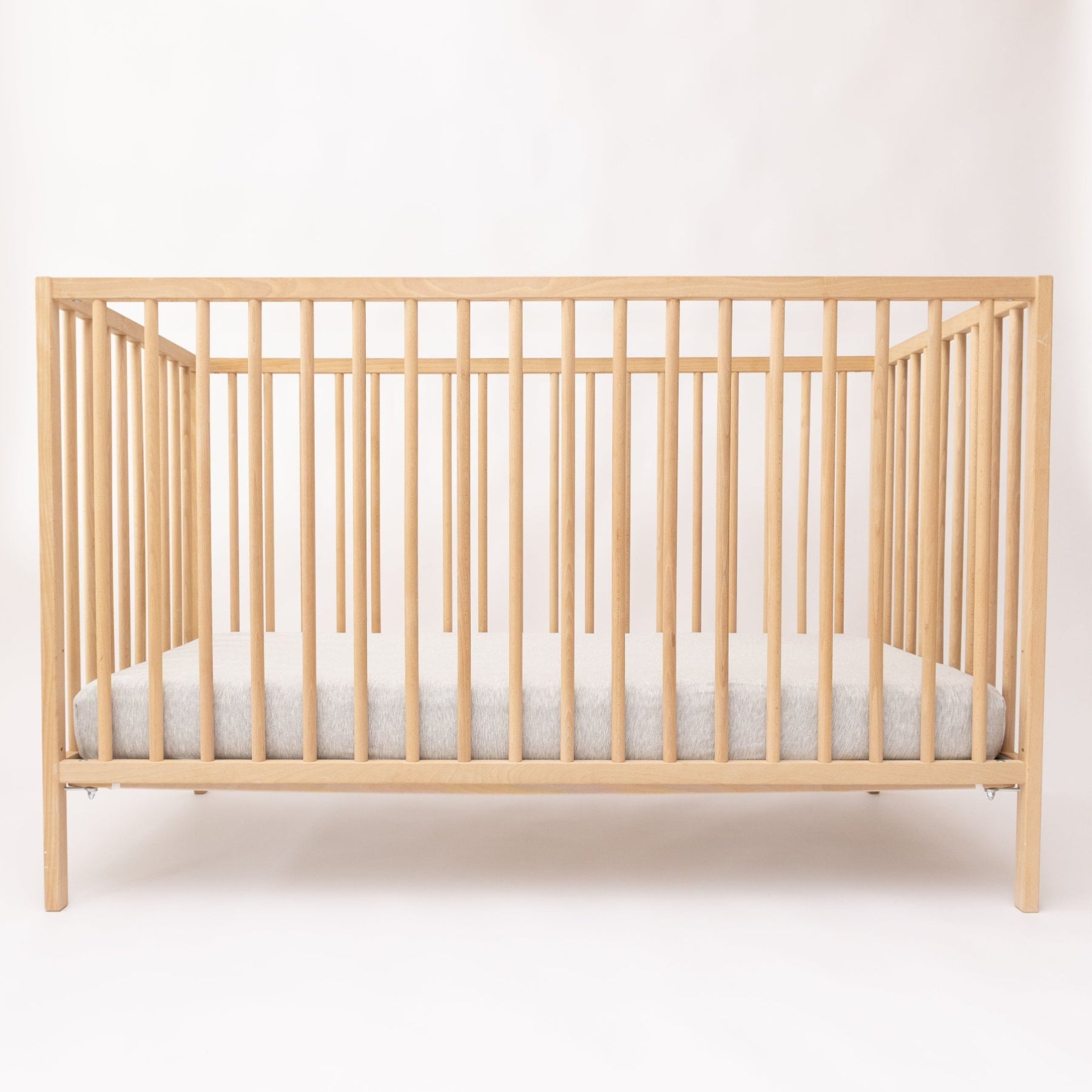 Wooden crib with a gray mattress on a white background
