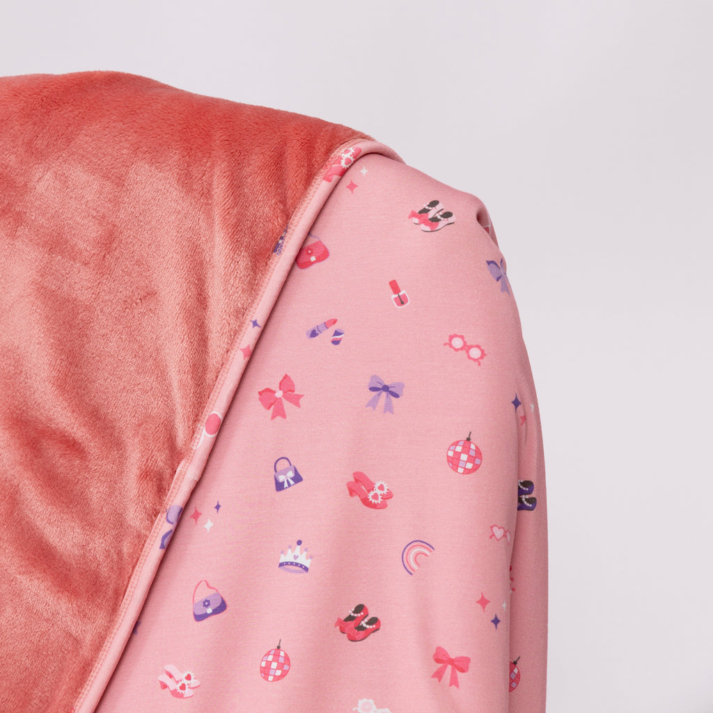 Close up of a pink blanket with small girly patterns draped over a chair on a white background