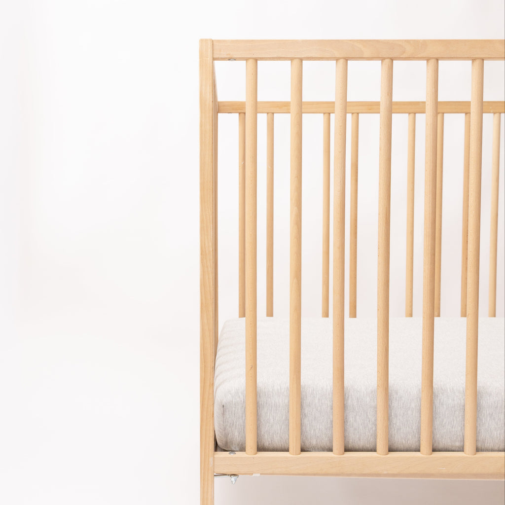 Wooden crib with gray mattress on a white background