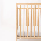 Wooden crib with gray mattress on a white background