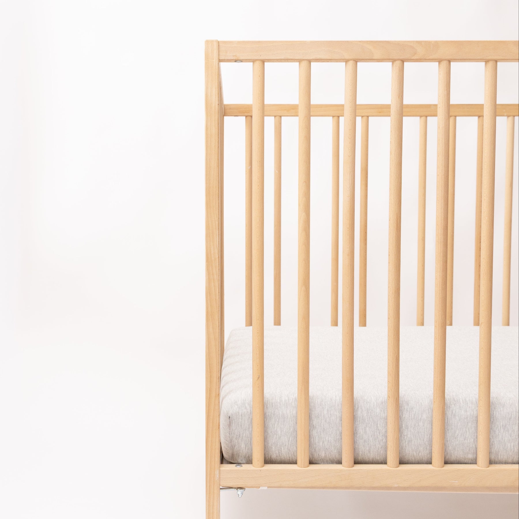 Wooden crib with gray mattress on a white background