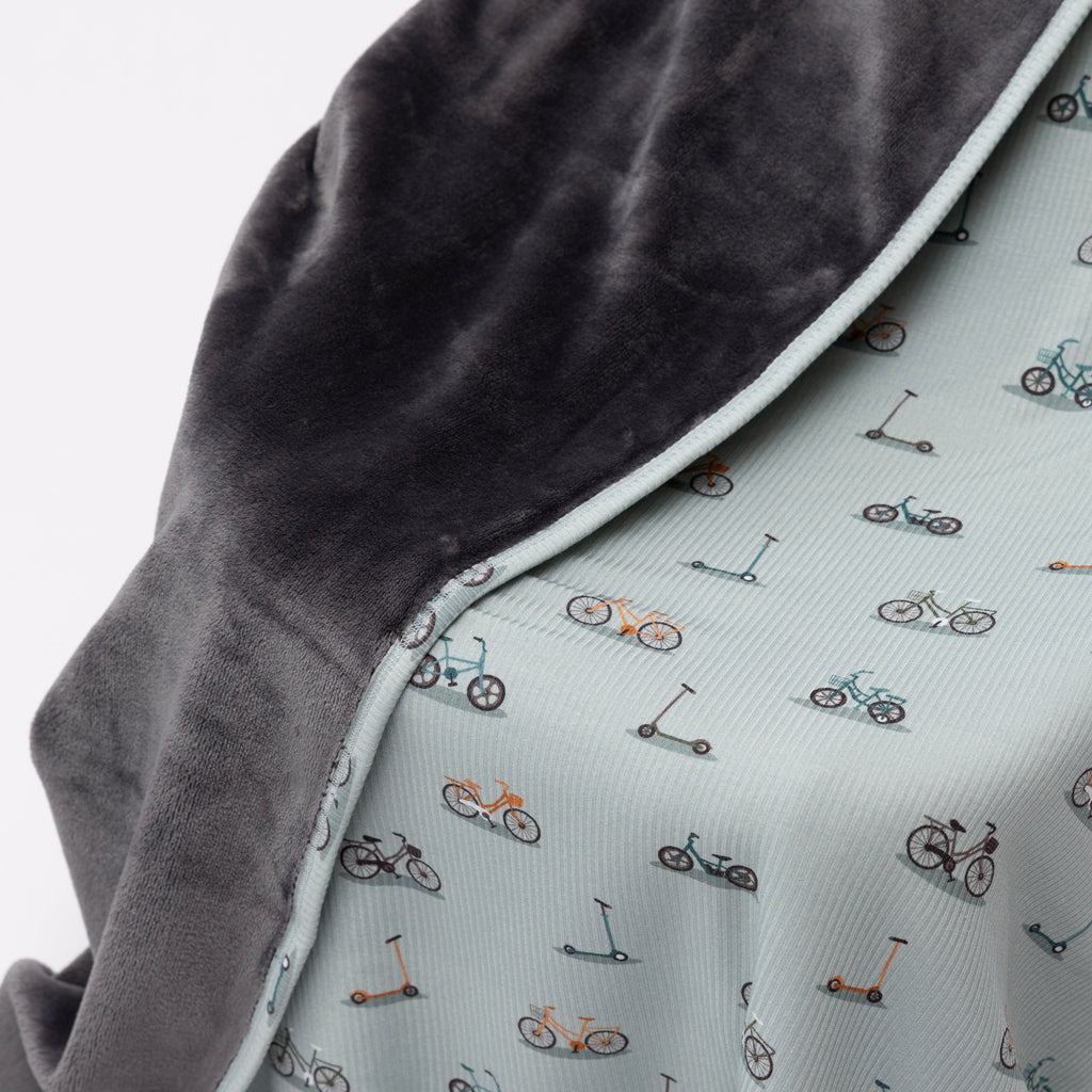 Close up of children's blanket with bicyles & scooters pattern draped on a wooden chair