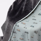 Close up of children's blanket with bicyles & scooters pattern draped on a wooden chair