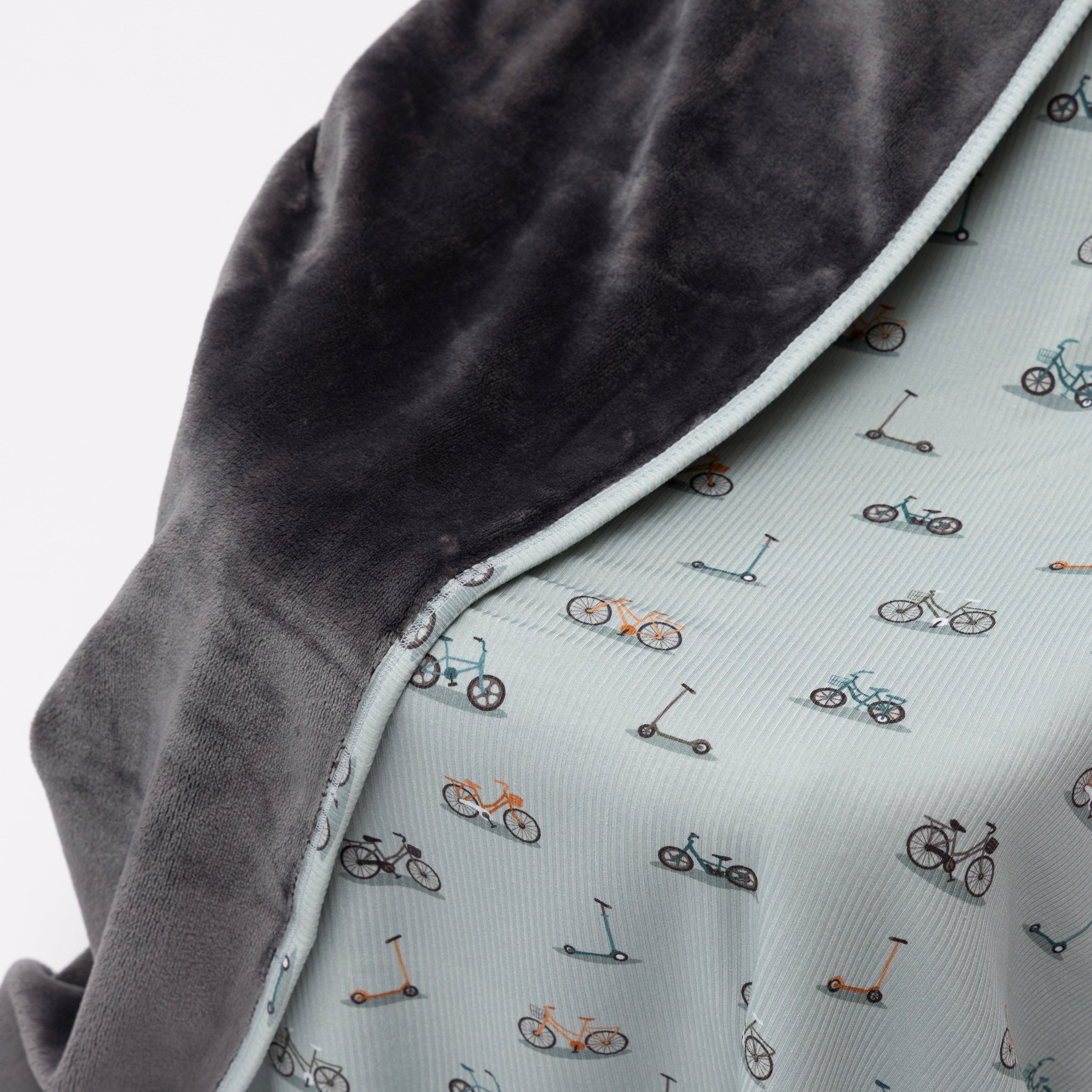 Close up of children's blanket with bicyles & scooters pattern draped on a wooden chair