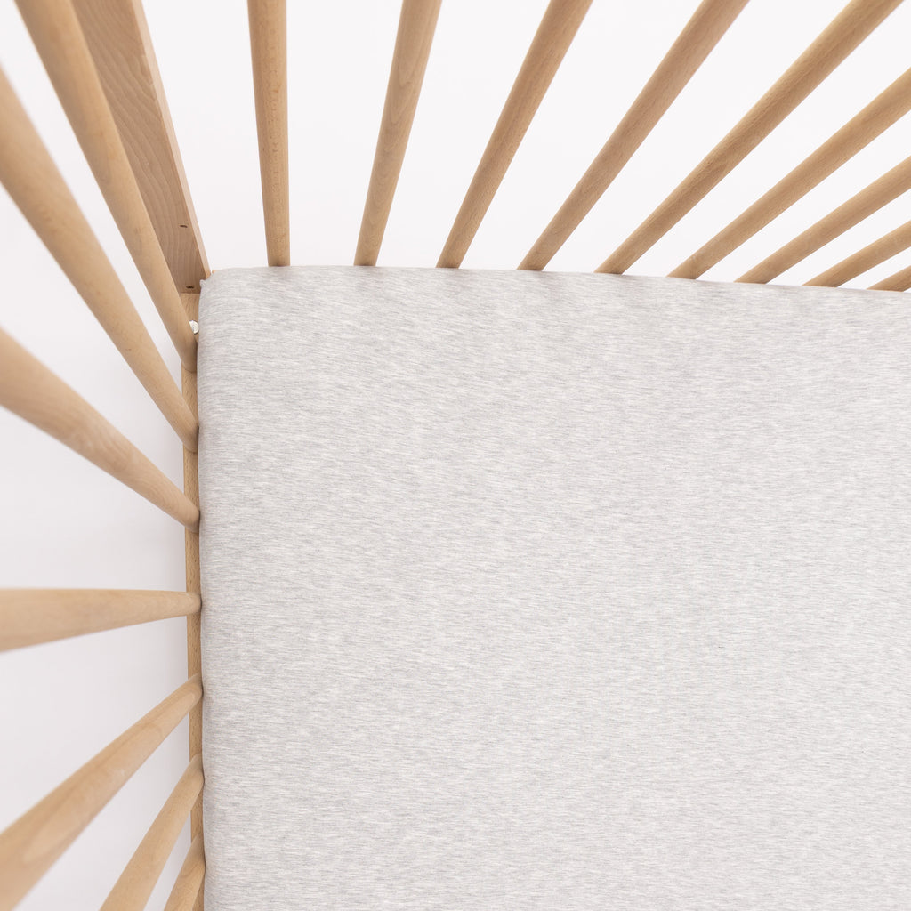 Close-up of a textured gray fabric against a wooden crib frame.