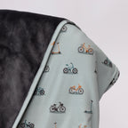 Close up of children's blanket with bicyles & scooters pattern draped on a wooden chair