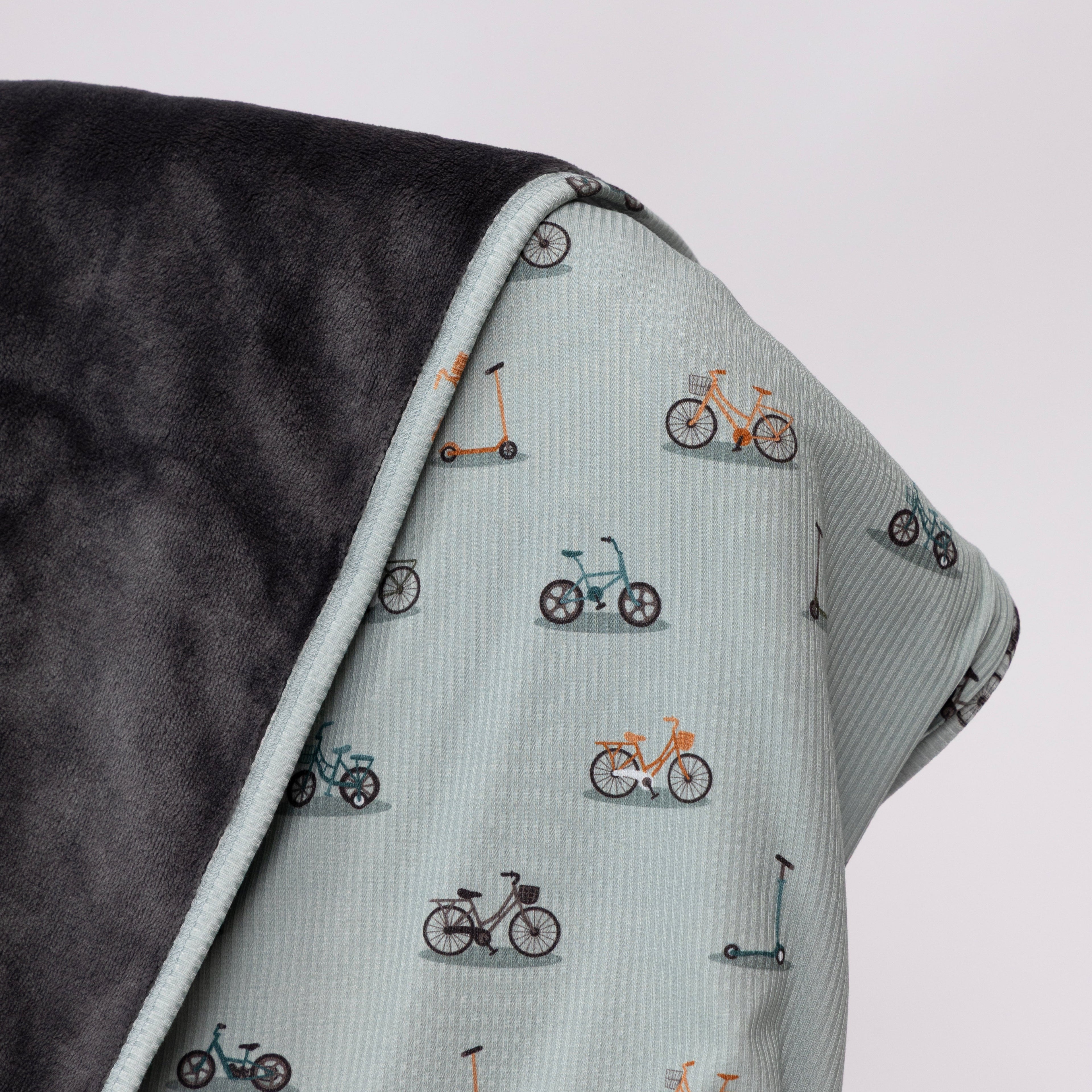 Close up of children's blanket with bicyles & scooters pattern draped on a wooden chair