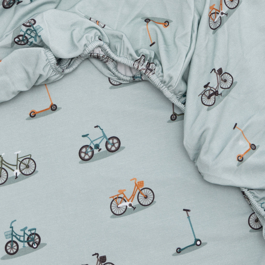 Light blue fabric with bicycle and scooter patterns, with a close-up of a fitted sheet.