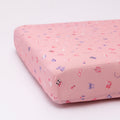 Pink crib sheet with colorful girly patterns on a white background