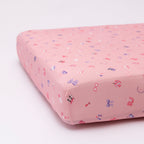 Pink crib sheet with colorful girly patterns on a white background