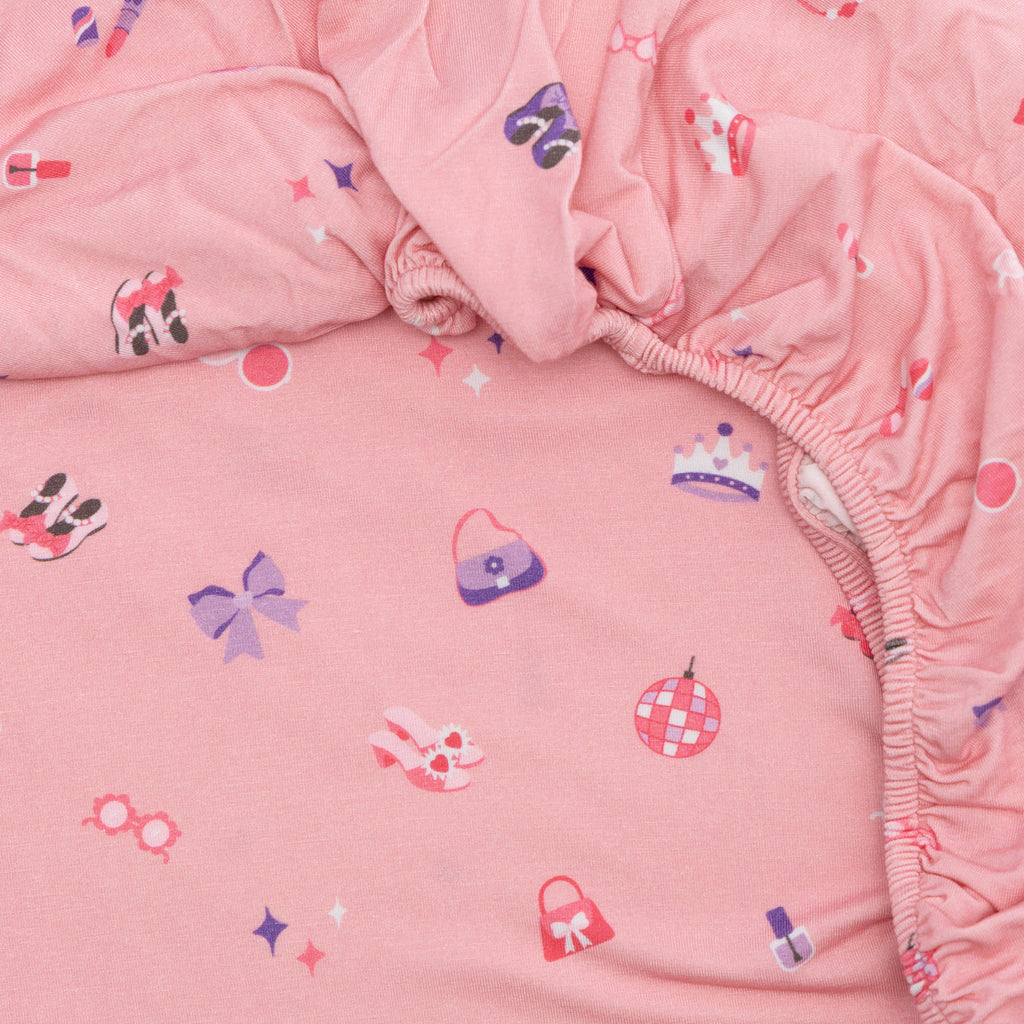 Close-up of pink fabric with colorful girly patterns, likely from a children's bedding set.