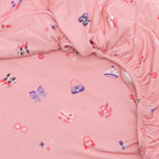 Close-up of pink fabric with colorful girly patterns, likely from a children's bedding set.