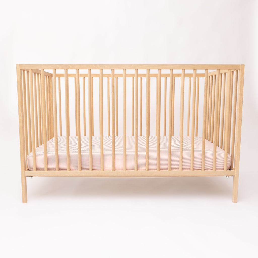 Wooden crib with pink striped sheet on a white background