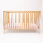 Wooden crib with pink striped sheet on a white background