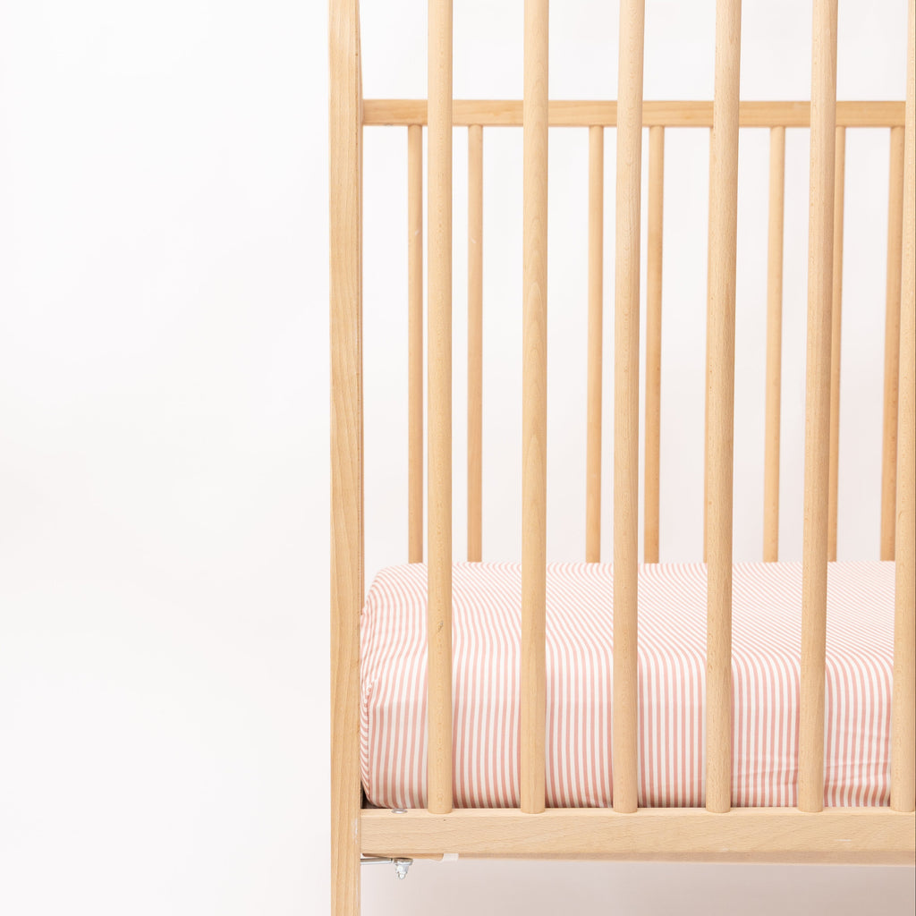 Wooden crib with pink striped sheet on a white background