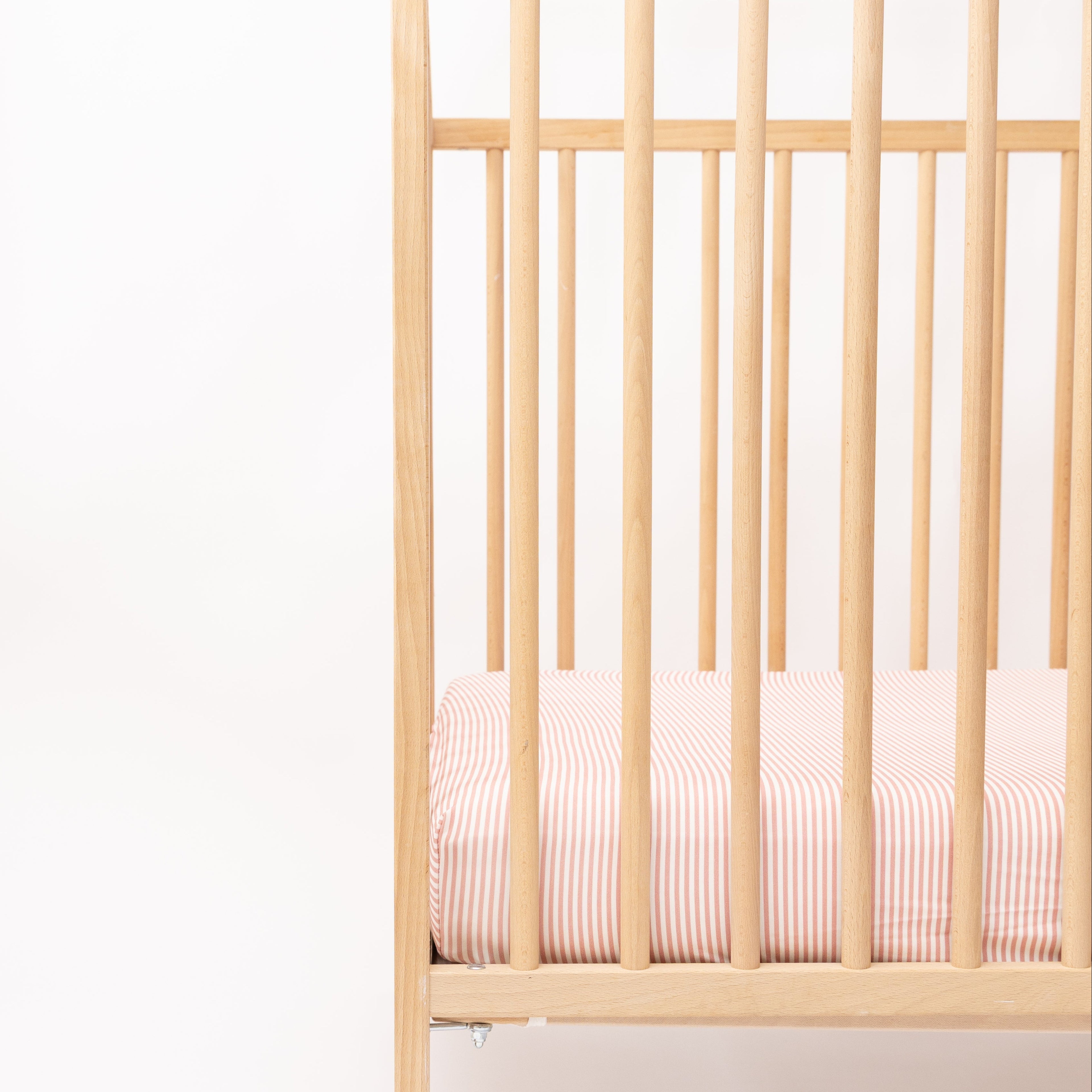 Wooden crib with pink striped sheet on a white background