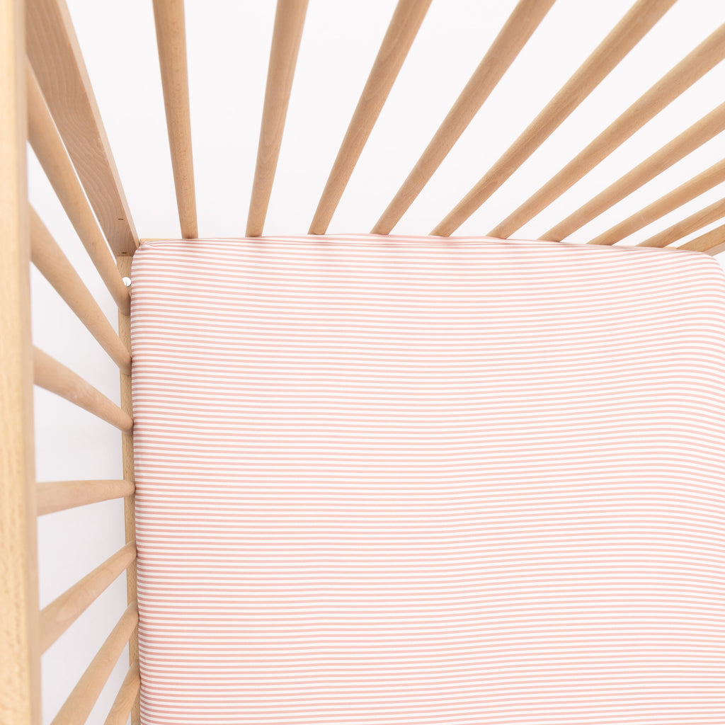 Wooden crib with a pink stripe fitted sheet on a white background