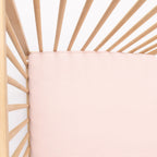 Wooden crib with a pink stripe fitted sheet on a white background