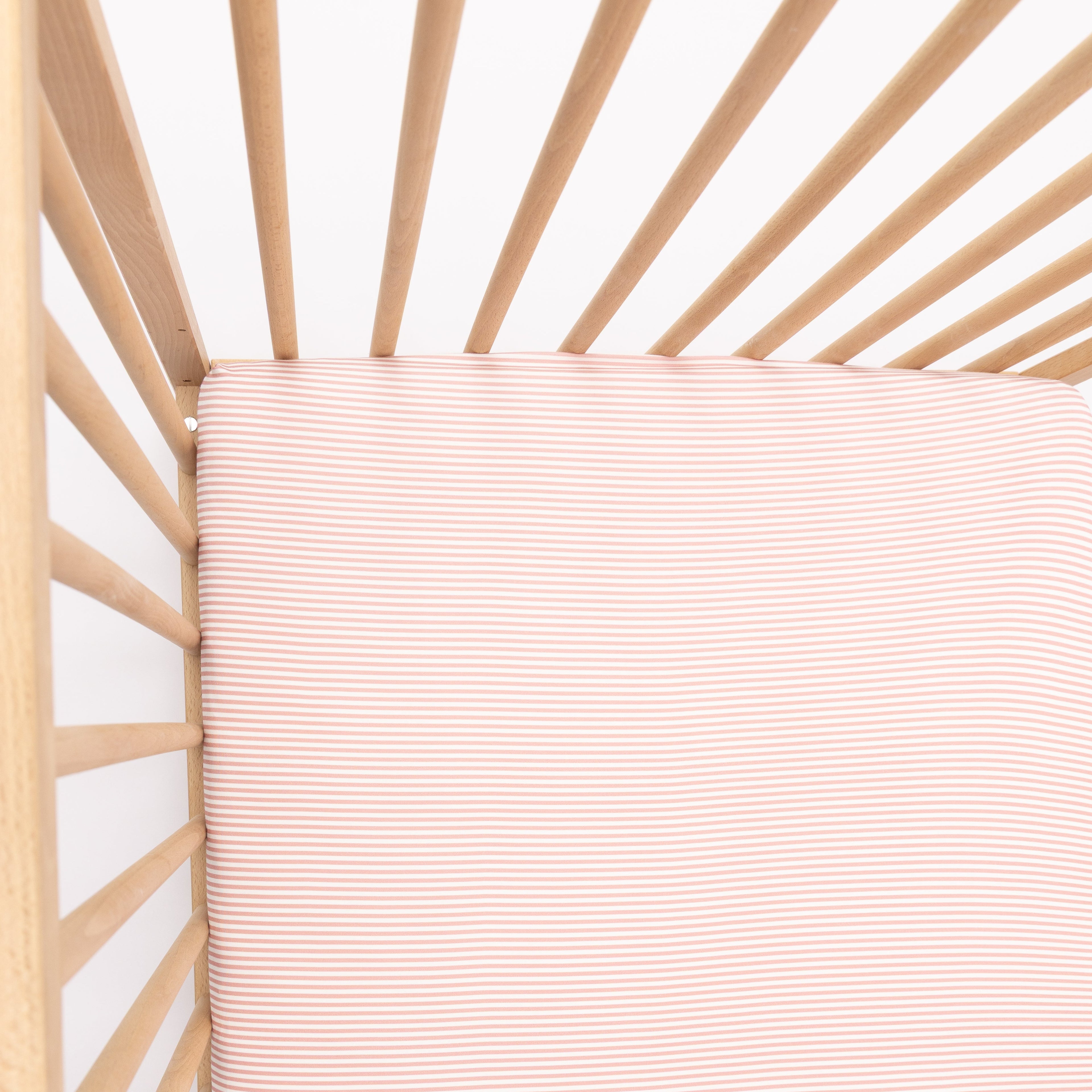 Wooden crib with a pink stripe fitted sheet on a white background