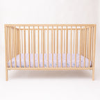 Wooden crib with a fitted sheet featuring colorful unicorn patterns on a light background