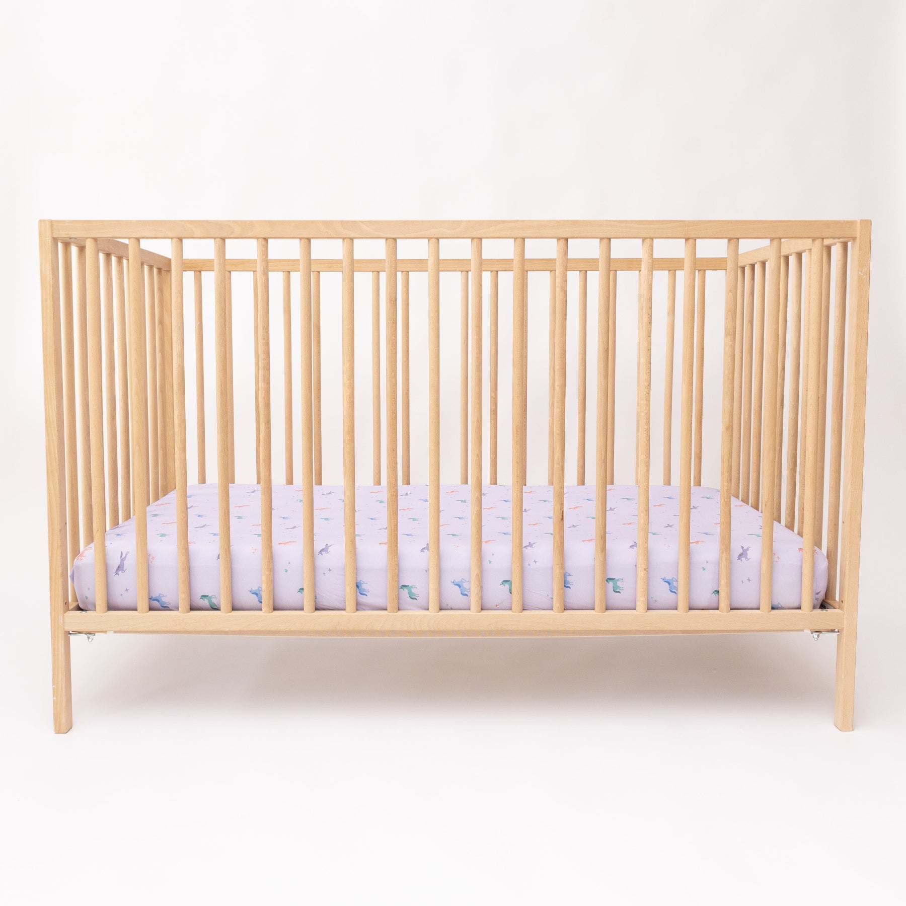 Wooden crib with a fitted sheet featuring colorful unicorn patterns on a light background