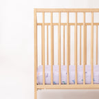 Wooden crib with a fitted sheet featuring colorful unicorn patterns on a light background
