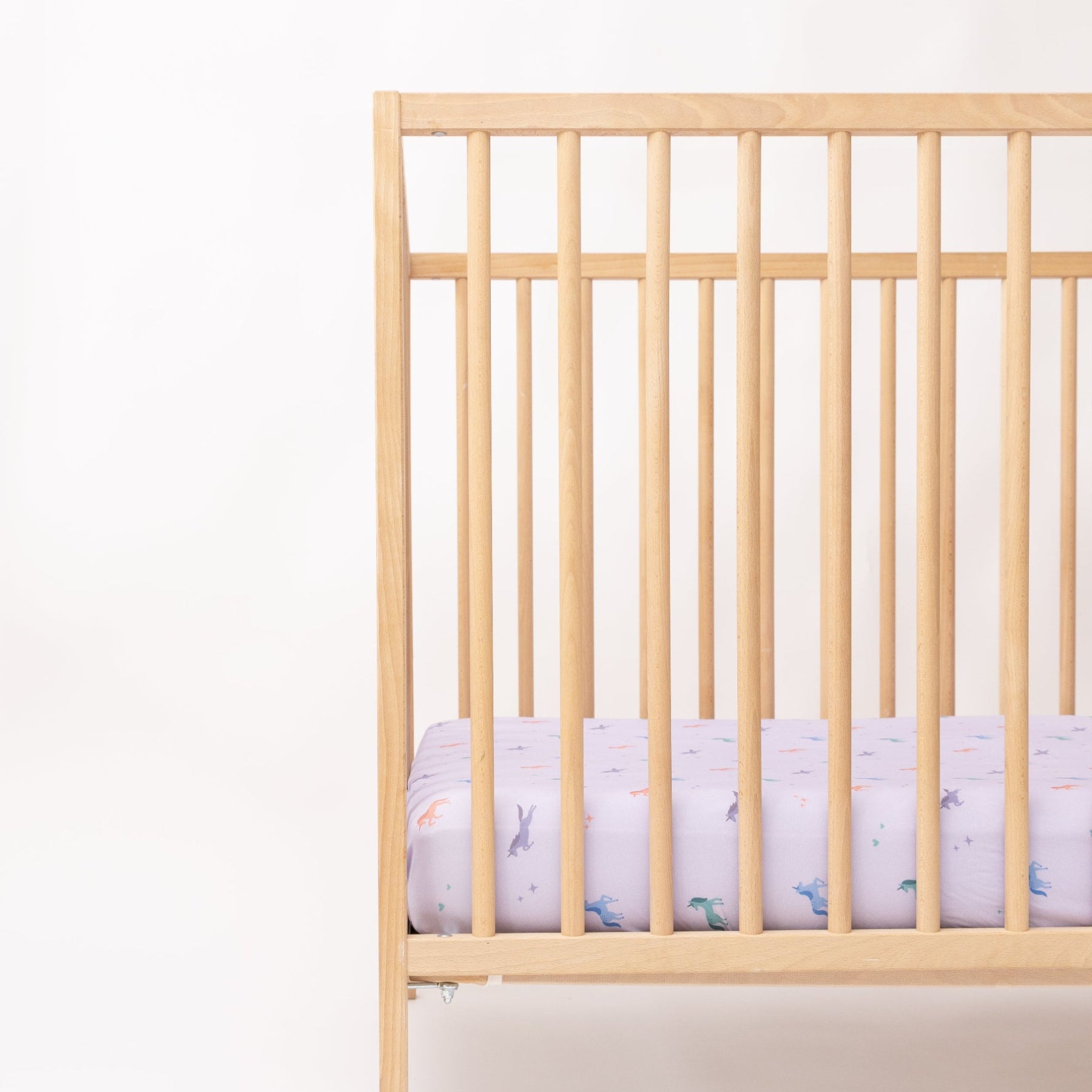 Wooden crib with a fitted sheet featuring colorful unicorn patterns on a light background