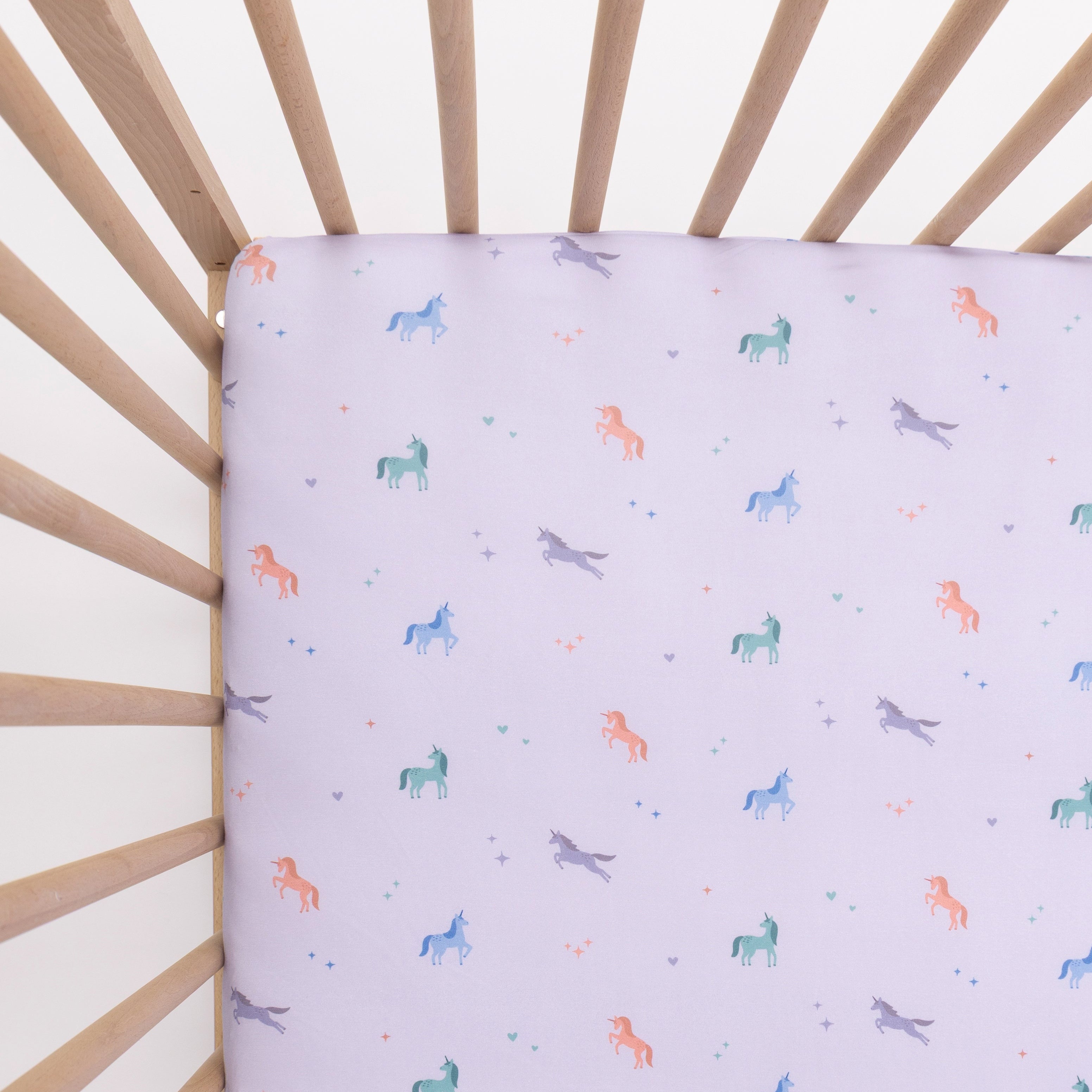 Crib with a fitted sheet featuring colorful unicorn patterns on a light background